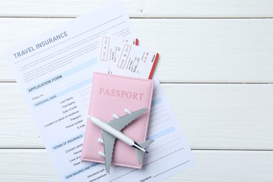 Photo of Medical tourism. Travel insurance application form, plane model, passport and flight tickets on white wooden table, top view. Space for text