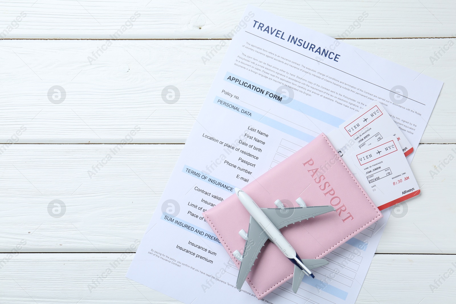 Photo of Medical tourism. Travel insurance application form, plane model, passport and flight tickets on white wooden table, top view. Space for text