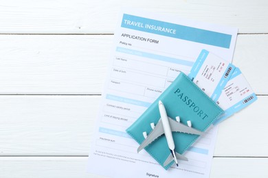 Photo of Medical tourism. Travel insurance application form, plane model, passport and flight tickets on white wooden table, top view. Space for text