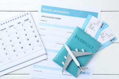 Photo of Medical tourism. Travel insurance application form, plane model, passport, flight tickets and calendar on white wooden table, flat lay