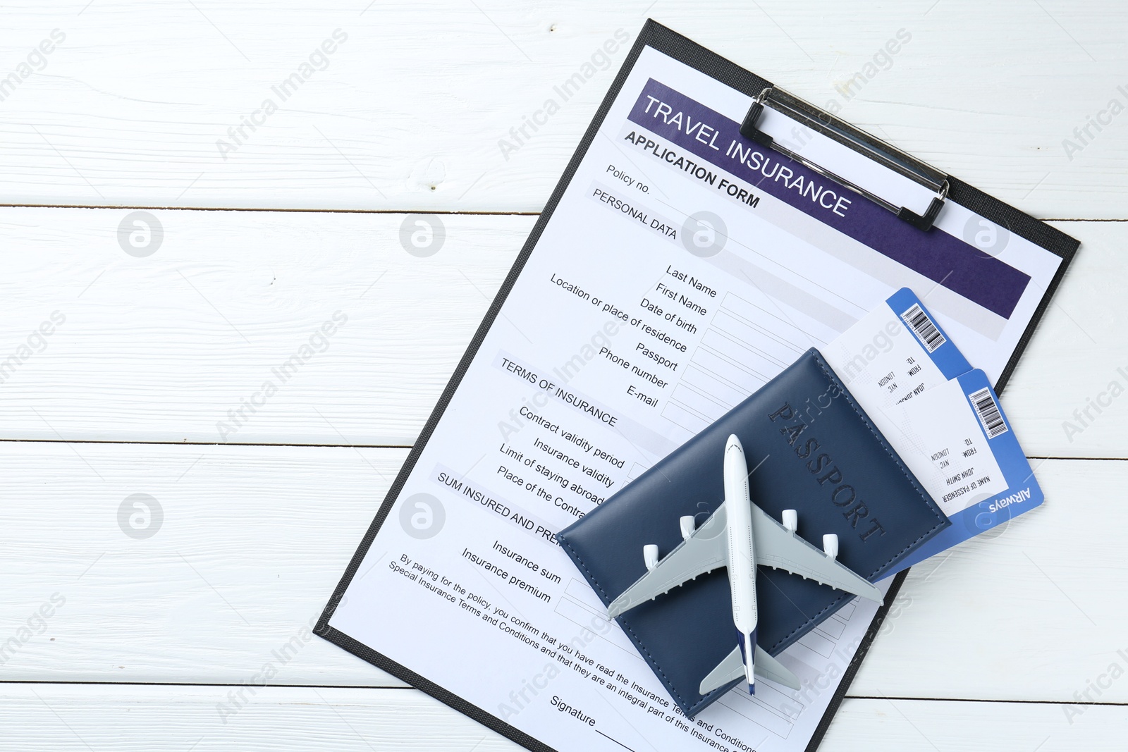 Photo of Medical tourism. Travel insurance application form, plane model, passport and flight tickets on white wooden table, top view. Space for text