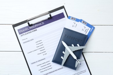 Photo of Medical tourism. Travel insurance application form, plane model, passport and flight tickets on white wooden table, top view