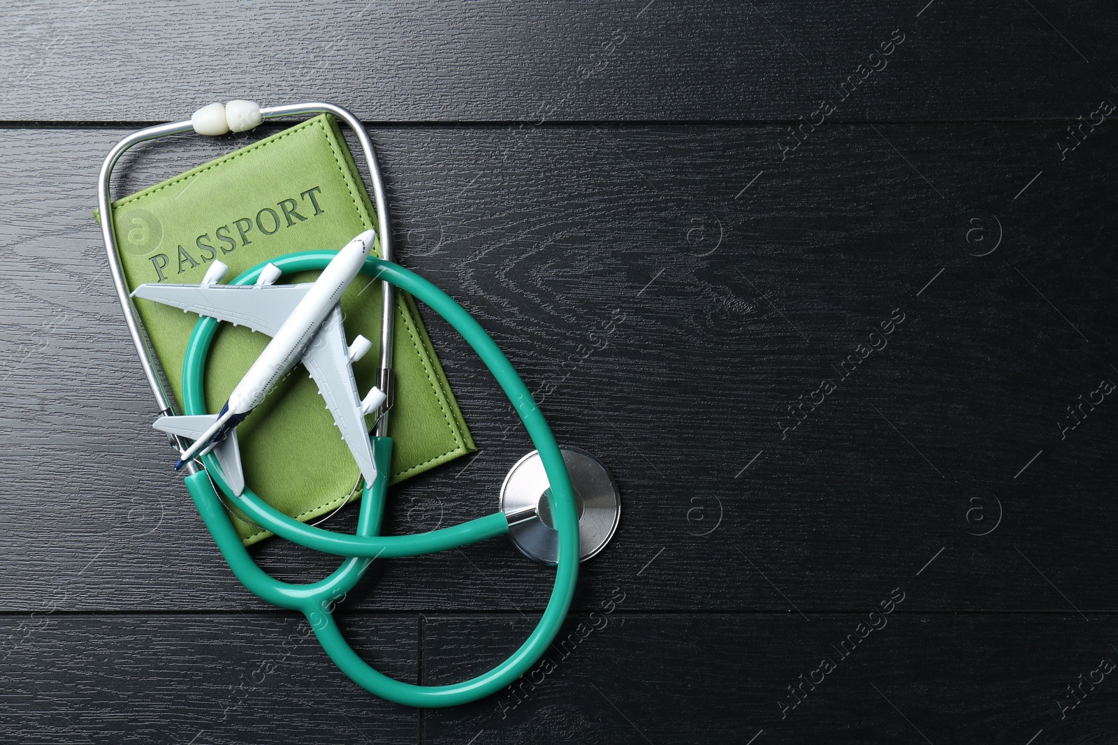 Photo of Medical tourism. Stethoscope, plane model and passport on black wooden table, top view. Space for text