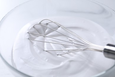 Photo of Whisk and whipped cream in bowl on white table, closeup