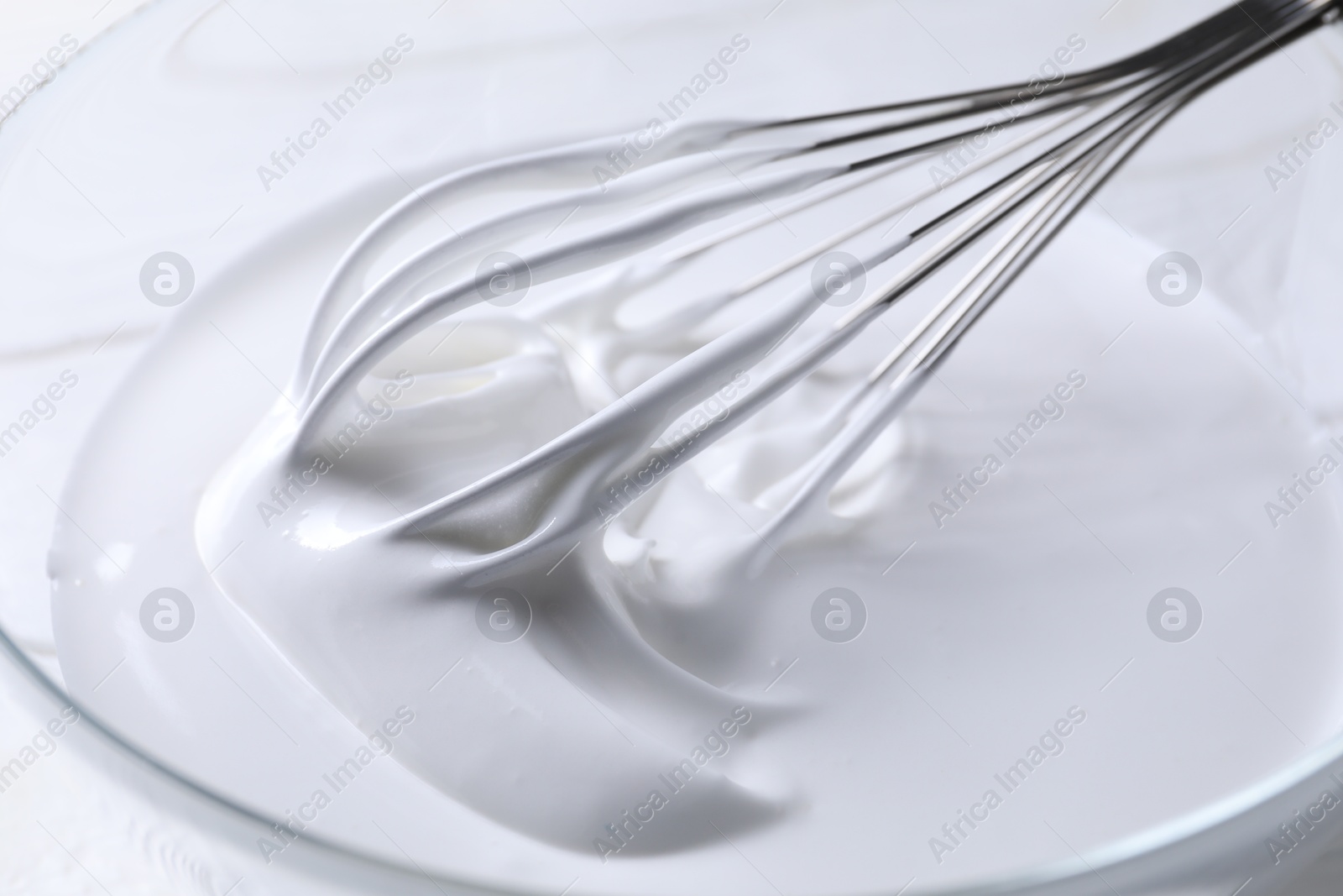 Photo of Whisk and whipped cream in bowl on table, closeup