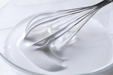 Photo of Whisk and whipped cream in bowl on table, closeup