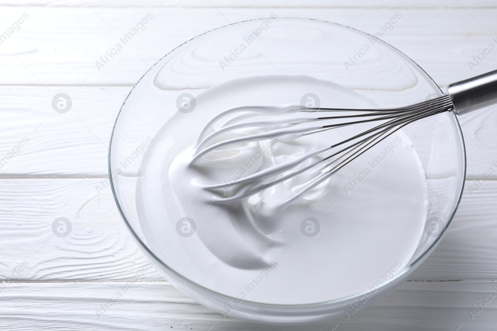 Photo of Whisk and whipped cream in bowl on white wooden table