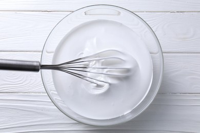 Photo of Whisk and whipped cream in bowl on white wooden table, top view