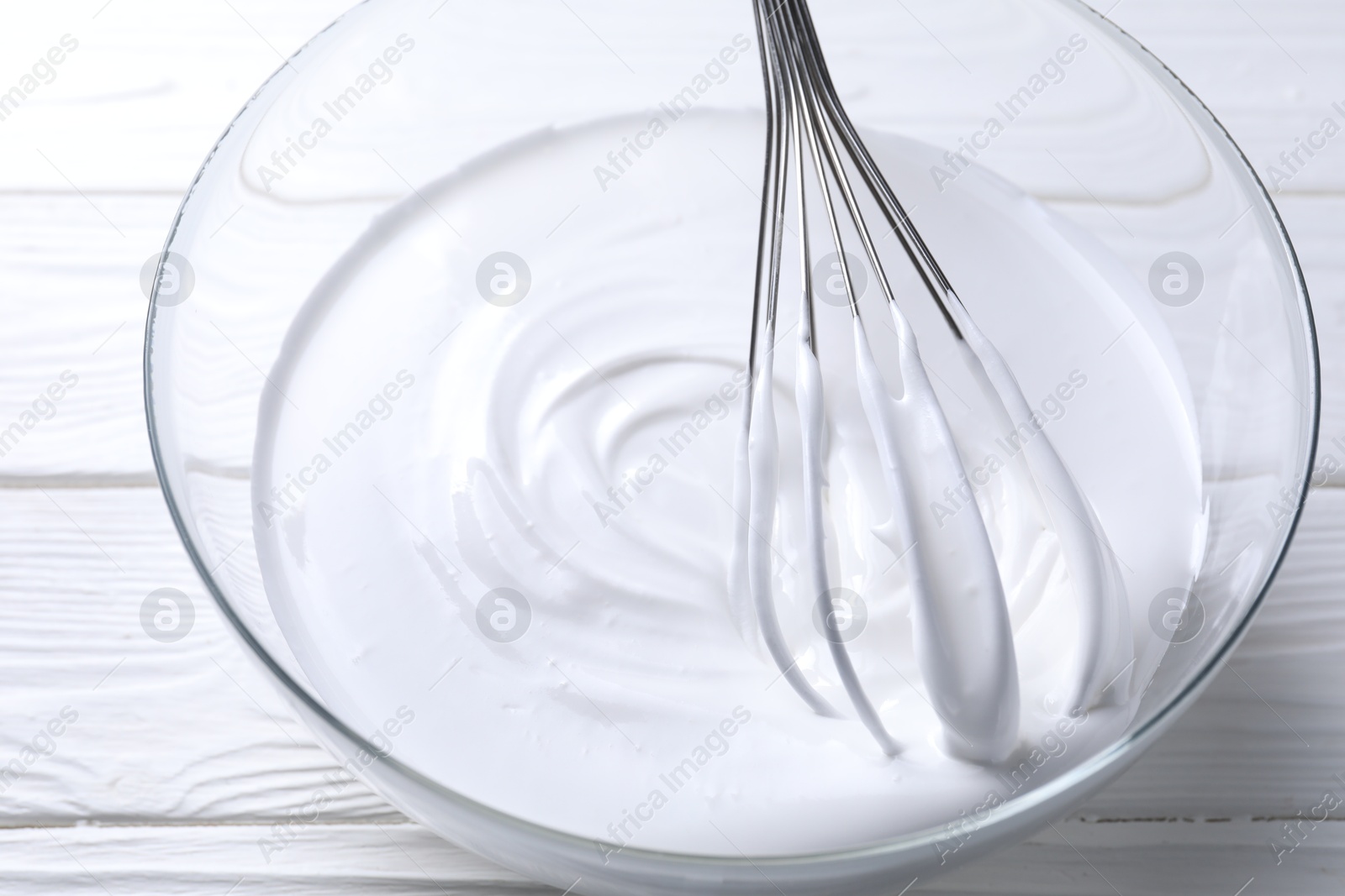 Photo of Whisk and whipped cream in bowl on white wooden table, closeup