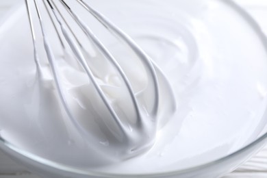 Photo of Whisk and whipped cream in bowl on table, closeup