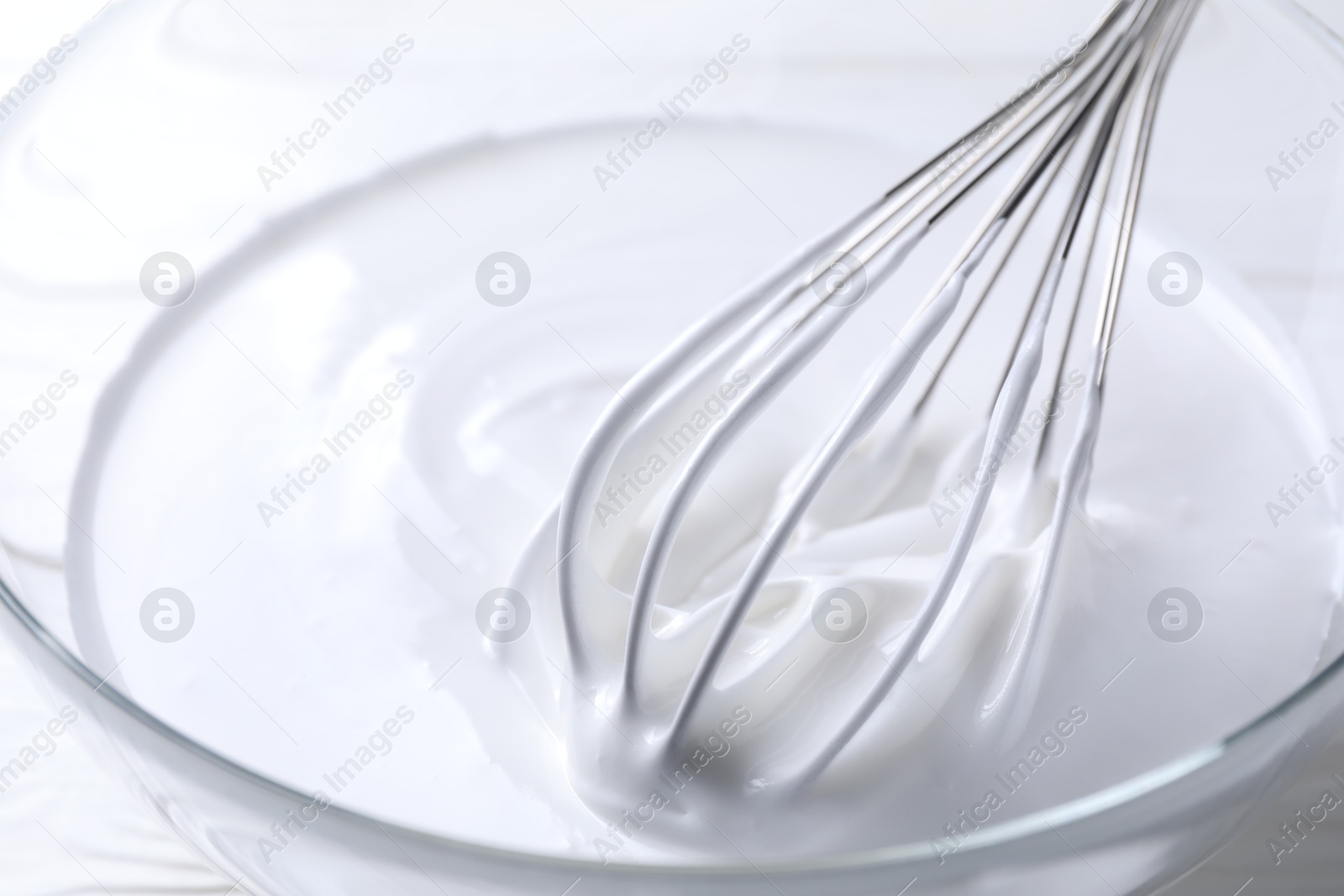 Photo of Whisk and whipped cream in bowl on table, closeup