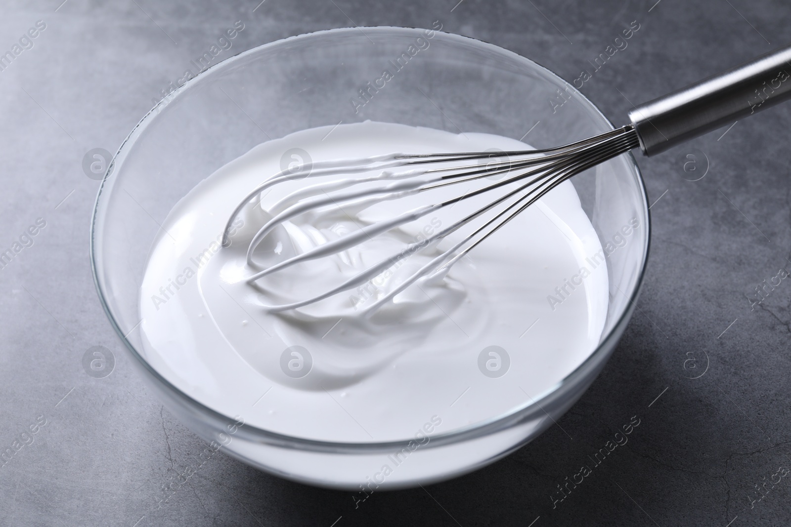 Photo of Whisk and whipped cream in bowl on grey table, closeup