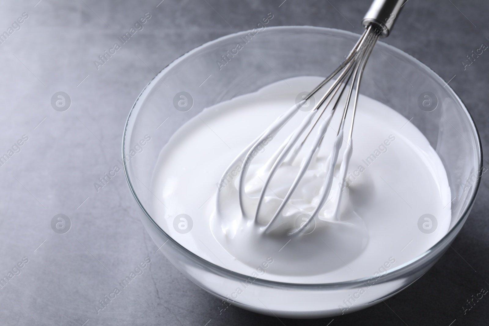 Photo of Whisk and whipped cream in bowl on grey table, closeup