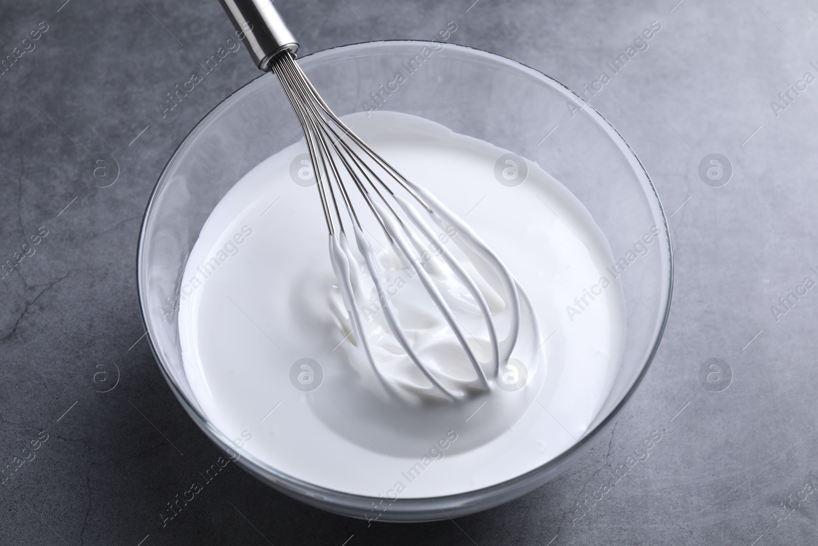 Photo of Whisk and whipped cream in bowl on grey table