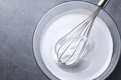 Photo of Whisk and whipped cream in bowl on grey table, top view