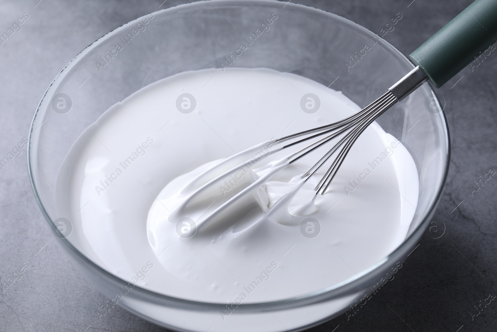 Photo of Whisk and whipped cream in bowl on grey table, closeup