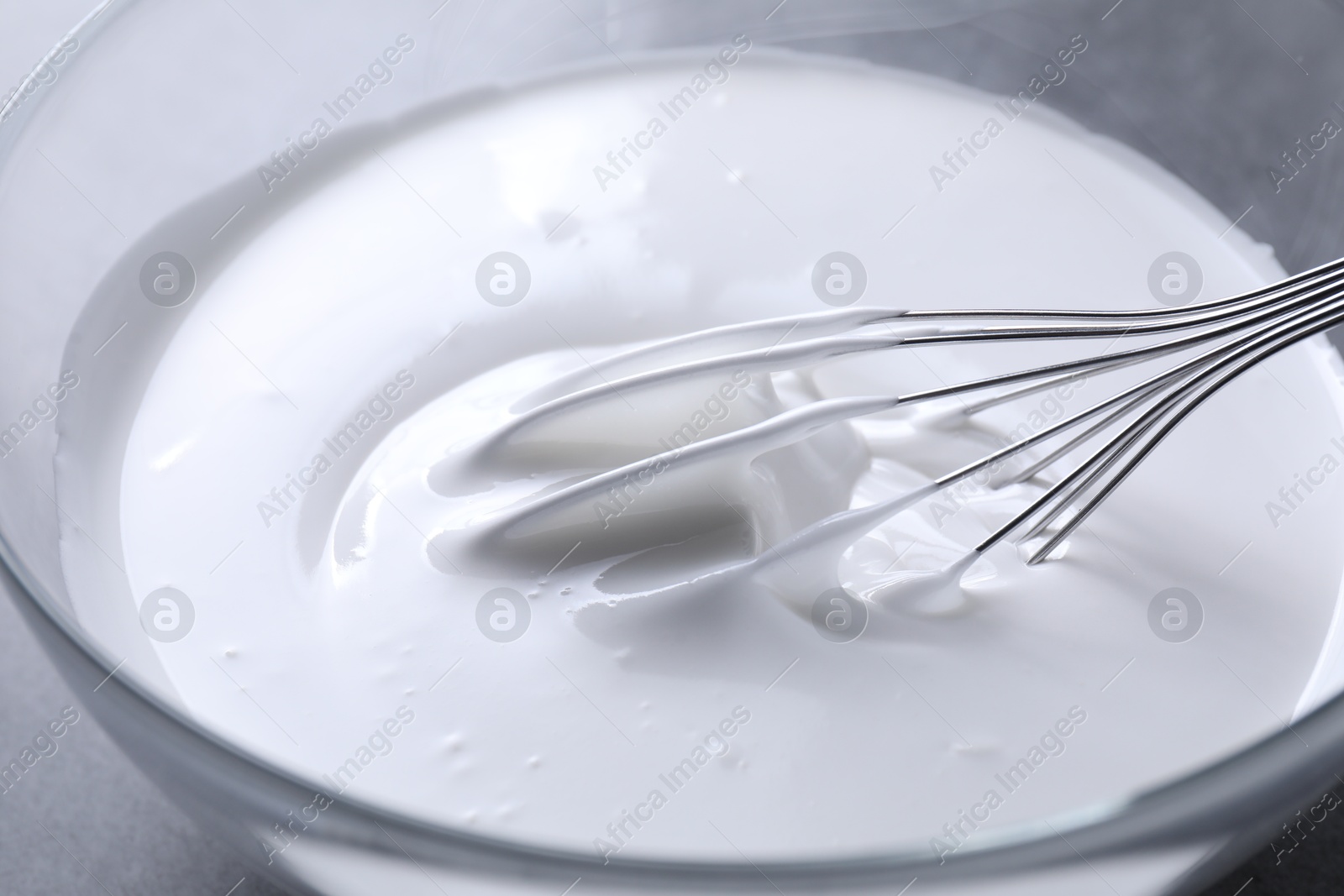 Photo of Whisk and whipped cream in bowl on grey table, closeup