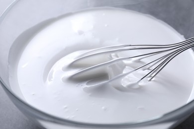 Photo of Whisk and whipped cream in bowl on grey table, closeup