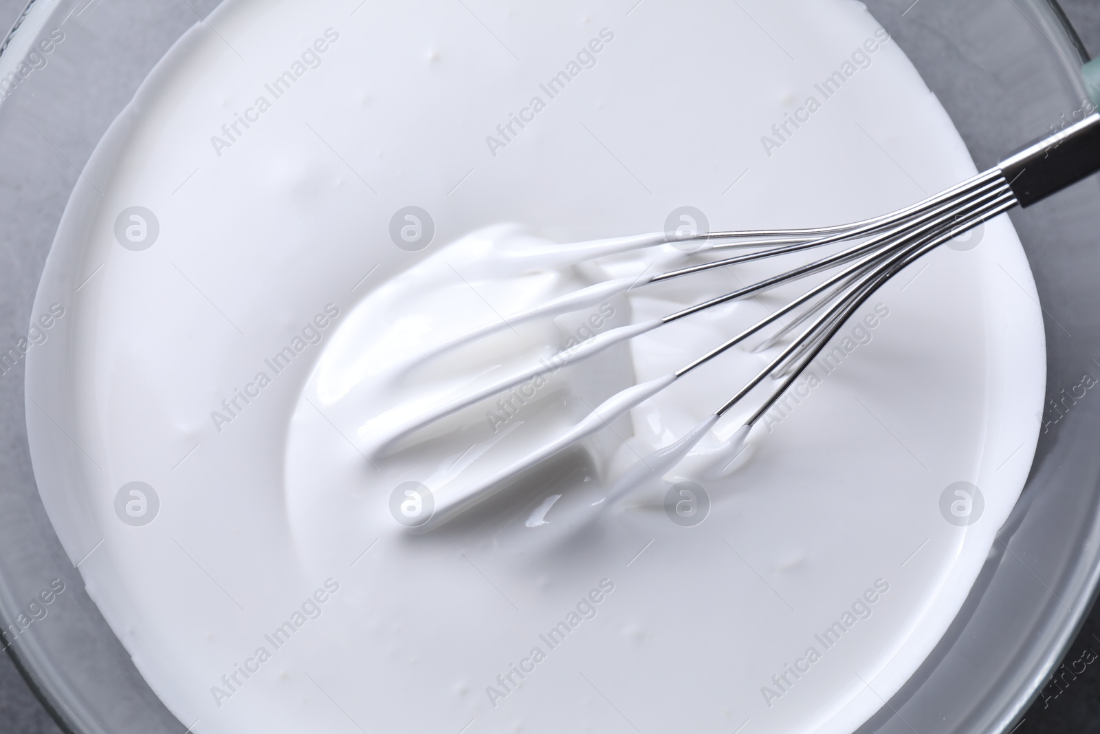 Photo of Whisk and whipped cream in bowl on grey table, top view