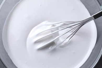 Photo of Whisk and whipped cream in bowl on grey table, top view