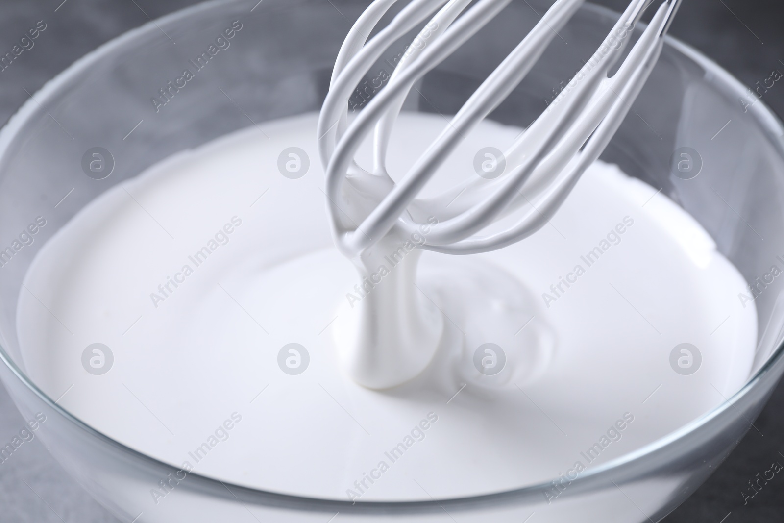 Photo of Mixing whipped cream in bowl with whisk on grey table, closeup