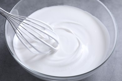 Photo of Mixing whipped cream in bowl with whisk on grey table, closeup