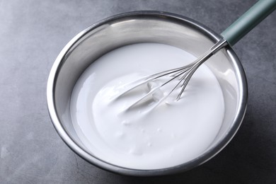 Photo of Whisk and whipped cream in bowl on grey table