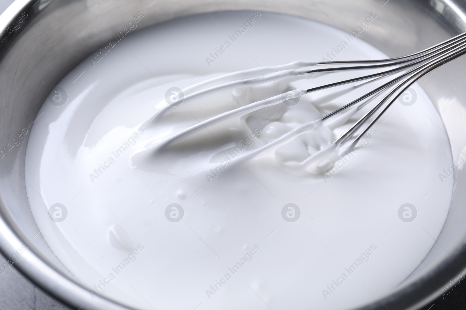 Photo of Whisk and whipped cream in bowl on table, closeup