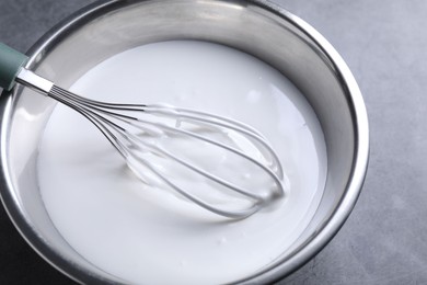 Photo of Whisk and whipped cream in bowl on grey table, closeup