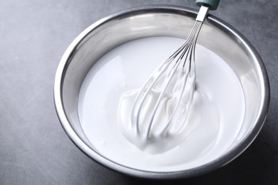 Photo of Whisk and whipped cream in bowl on grey table, closeup