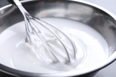 Photo of Whisk and whipped cream in bowl on table, closeup