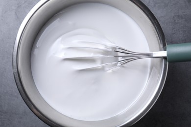 Photo of Whisk and whipped cream in bowl on grey table, top view