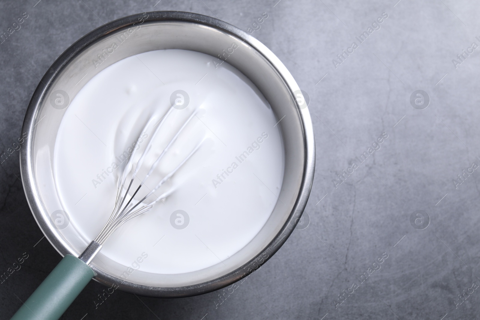 Photo of Whisk and whipped cream in bowl on grey table, top view. Space for text