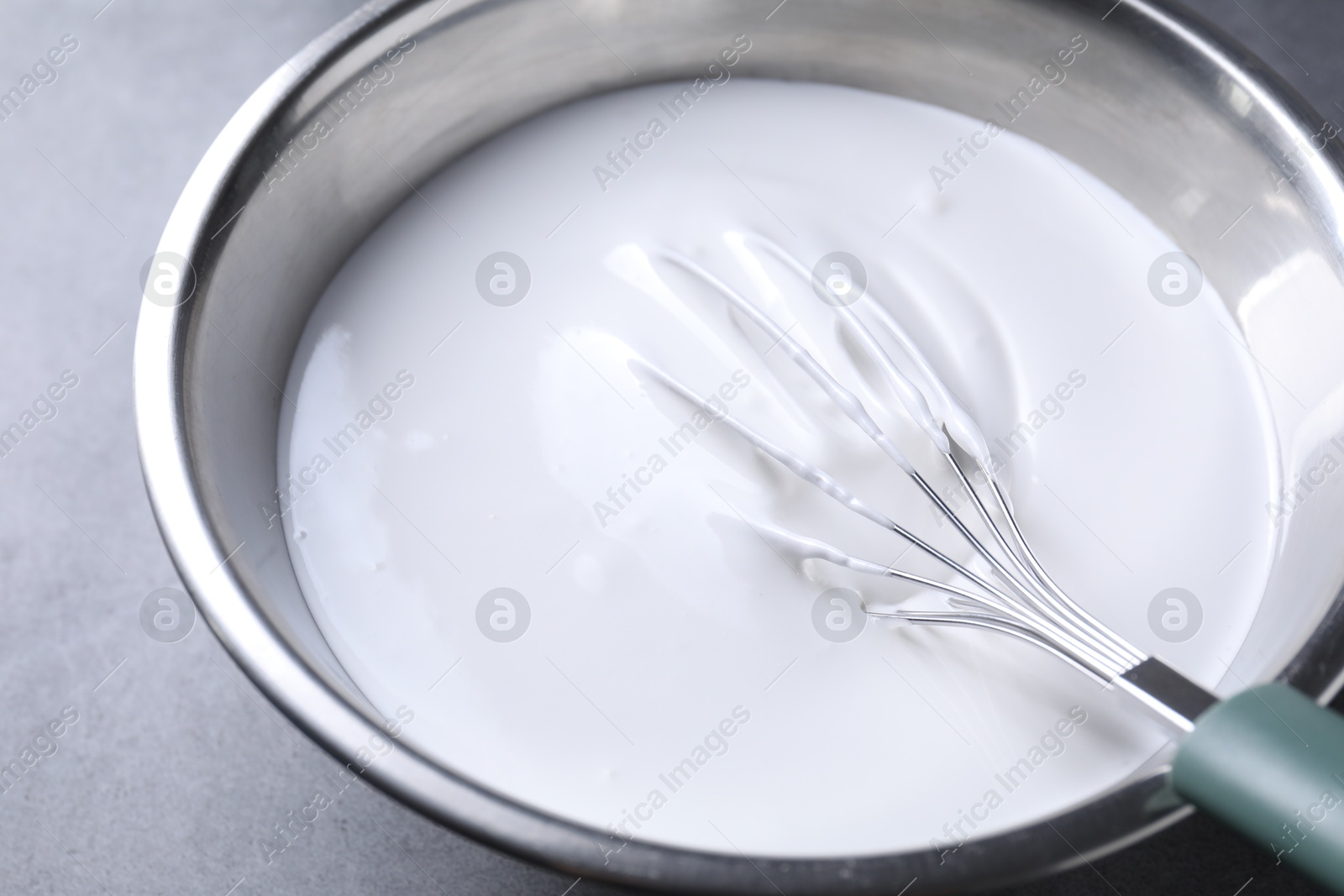 Photo of Whisk and whipped cream in bowl on grey table, closeup