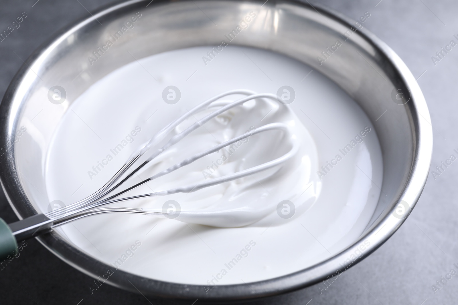 Photo of Whisk and whipped cream in bowl on grey table, closeup