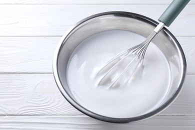 Photo of Whisk and whipped cream in bowl on white wooden table