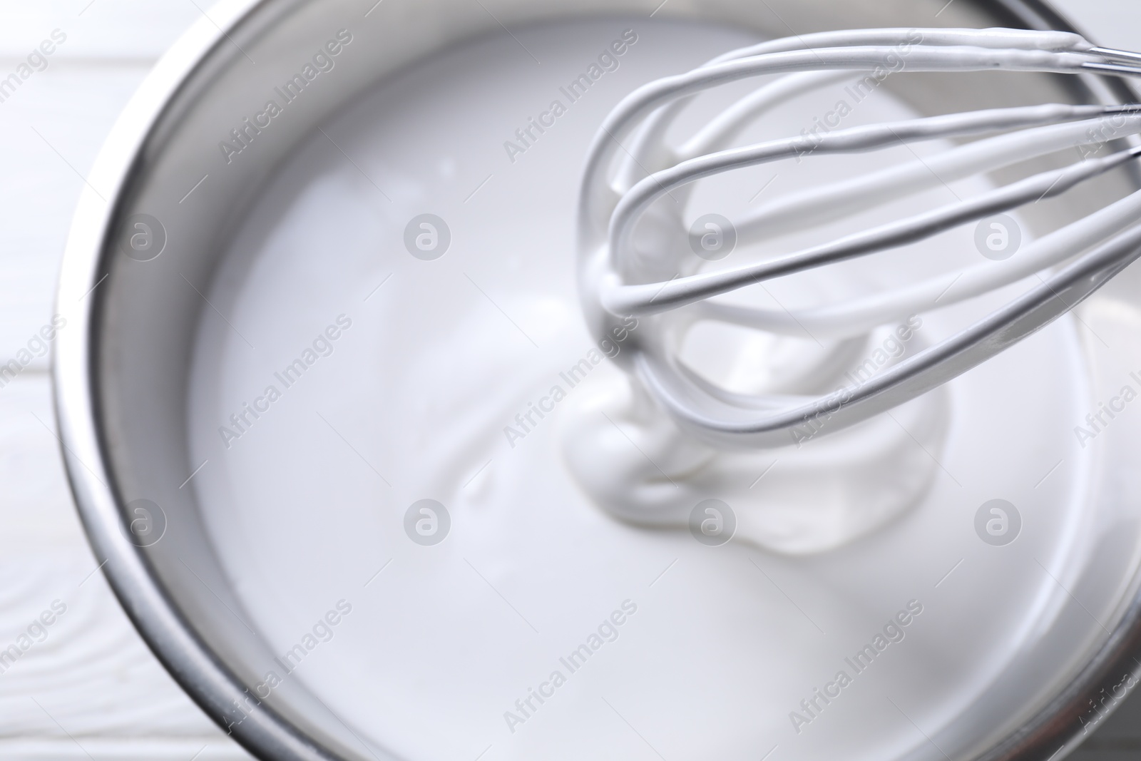 Photo of Mixing whipped cream in bowl with whisk on white table, above view