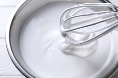 Photo of Mixing whipped cream in bowl with whisk on white table, above view