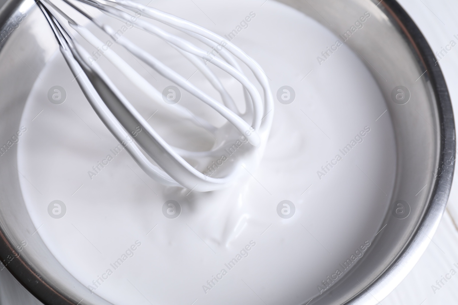 Photo of Mixing whipped cream in bowl with whisk on white table, above view