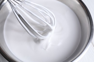 Photo of Mixing whipped cream in bowl with whisk on white table, above view