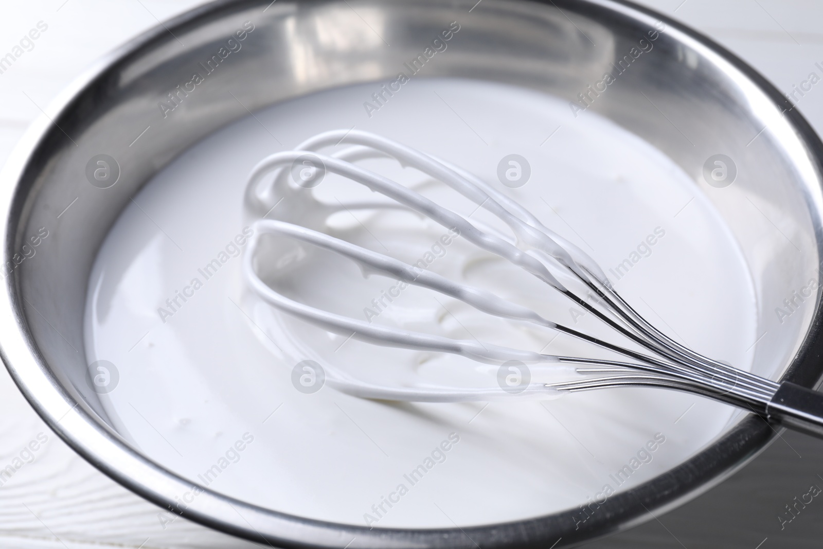 Photo of Whisk and whipped cream in bowl on white table, closeup