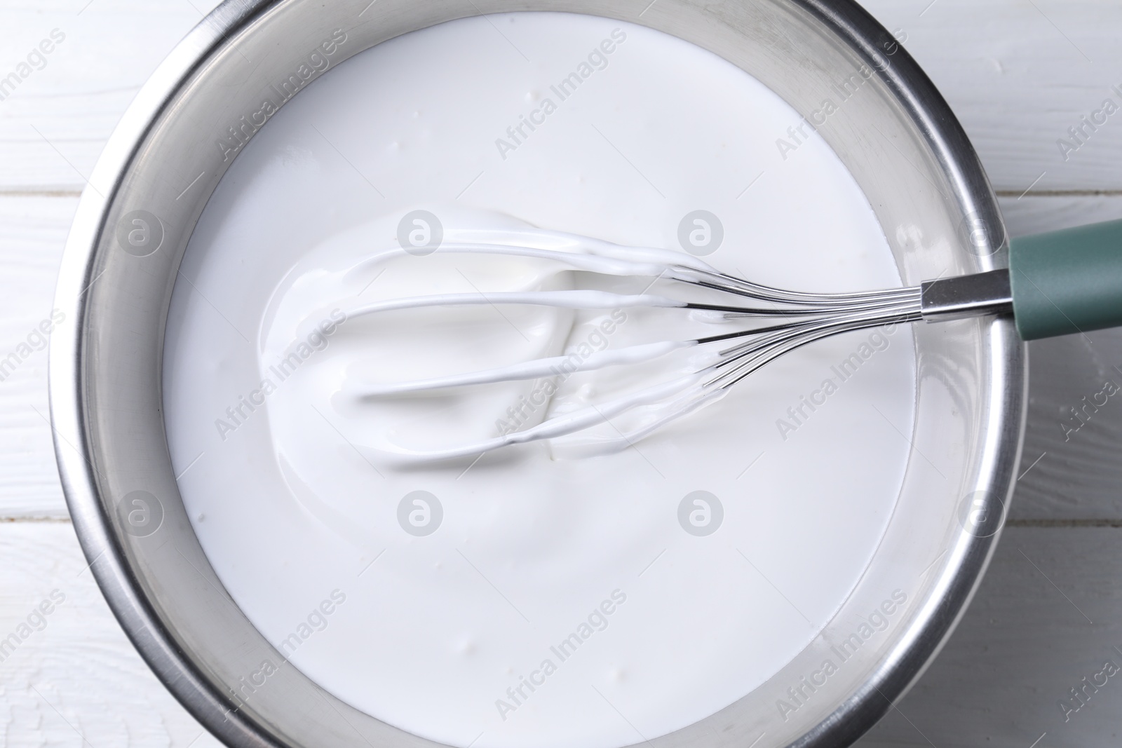 Photo of Whisk and whipped cream in bowl on white wooden table, top view