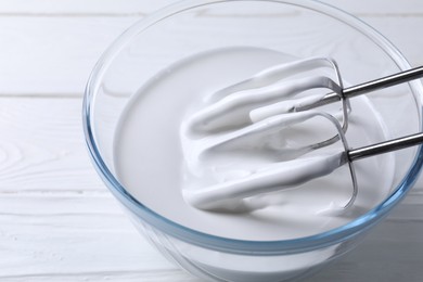 Photo of Mixing whipped cream with hand mixer in bowl on white wooden table, closeup