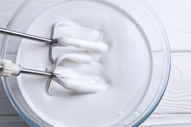 Photo of Mixing whipped cream with hand mixer in bowl on white wooden table, top view