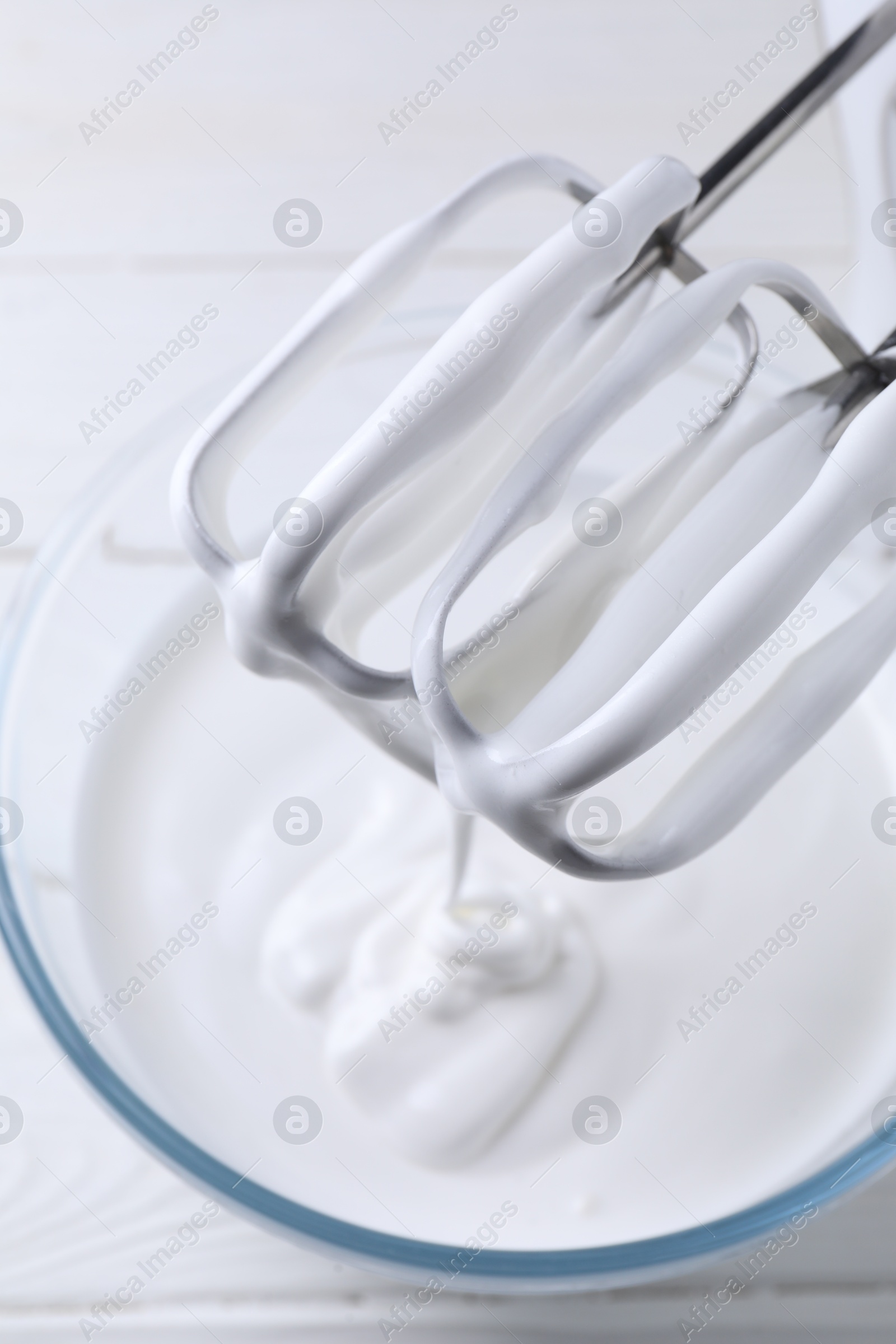 Photo of Mixing whipped cream with hand mixer in bowl on white wooden table, top view