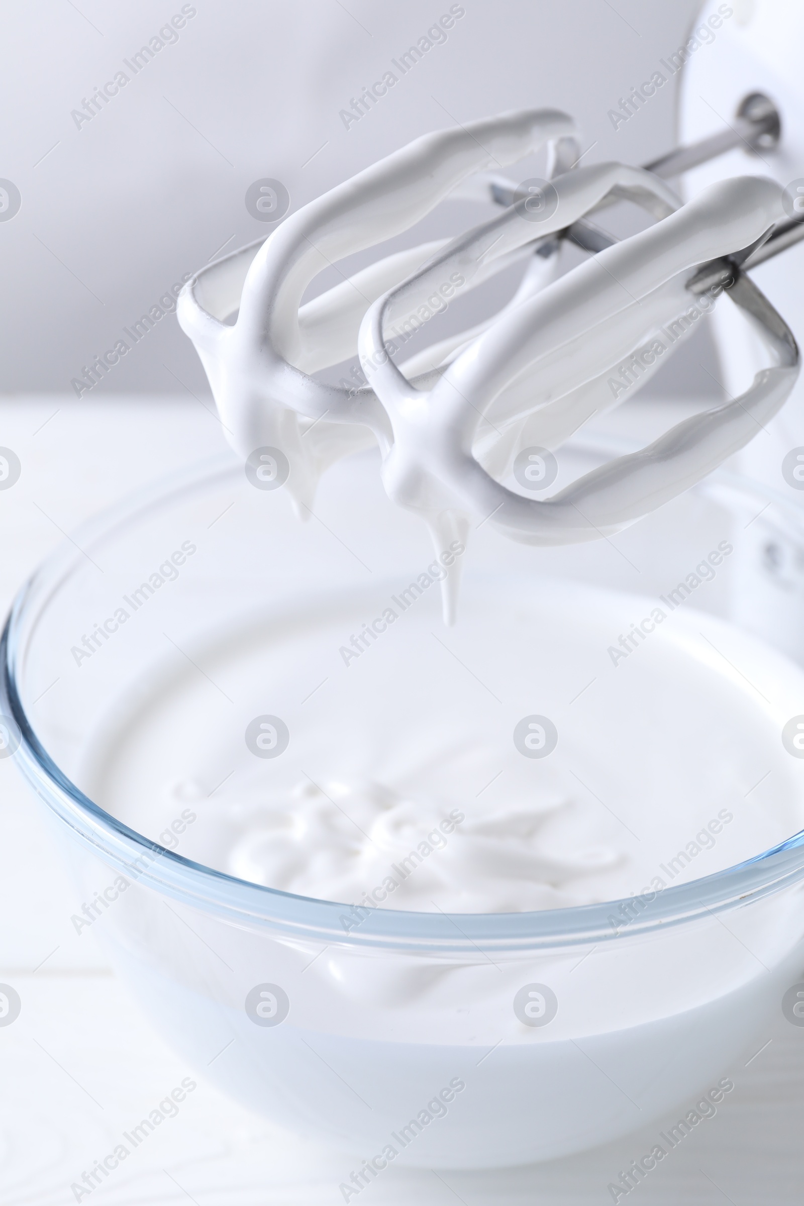 Photo of Hand mixer with whisks and bowl of whipped cream on white wooden table, closeup