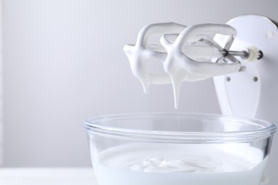 Photo of Hand mixer with whisks and bowl of whipped cream on white table, closeup. Space for text