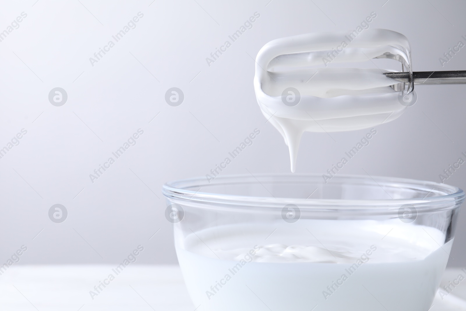 Photo of Hand mixer with whisks and bowl of whipped cream on white table, closeup. Space for text