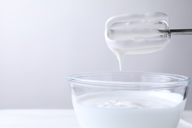 Photo of Hand mixer with whisks and bowl of whipped cream on white table, closeup. Space for text