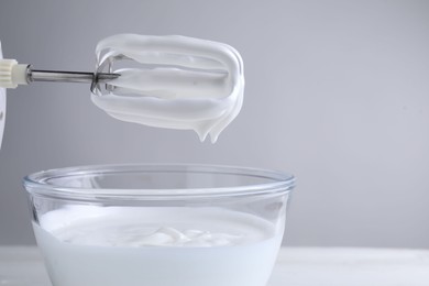 Photo of Hand mixer with whisks and bowl of whipped cream on white table, closeup. Space for text